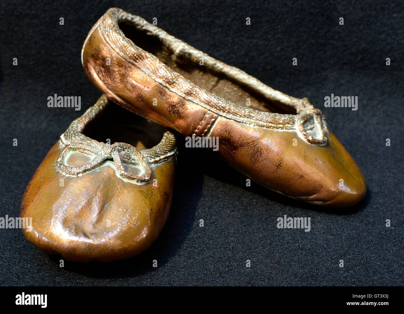 Her first ballet shoes. Copper toddler ballet shoes. Dancing shoes. Baby ballet shoes. Pair crossed in L shape. Stock Photo