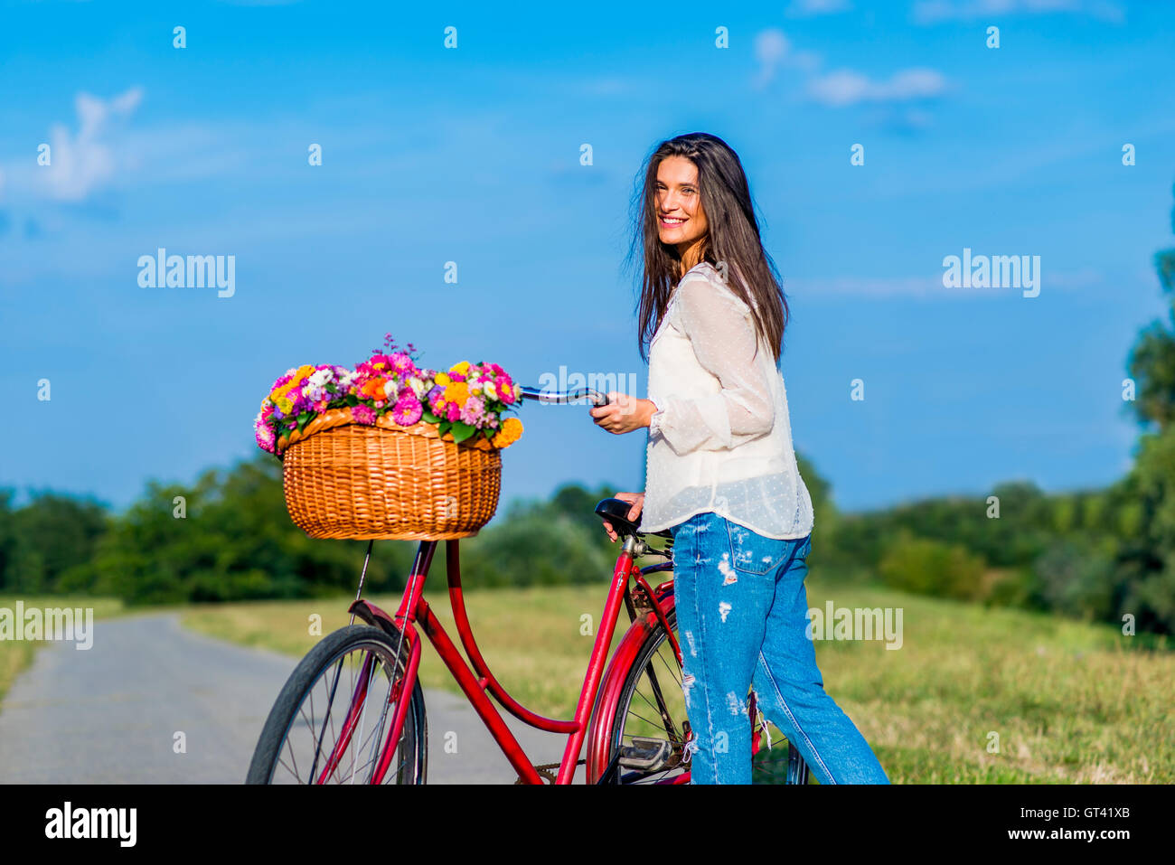 Young girl posing by a bicycle with a basket full of flowers Stock Photo