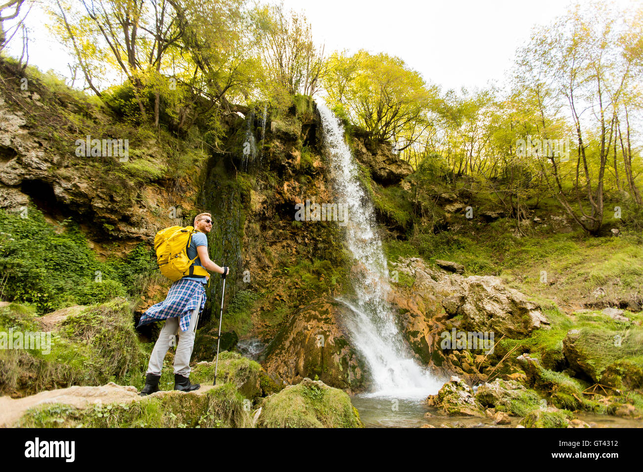 Young hiker stopped beside a mountain waterfall to rest Stock Photo