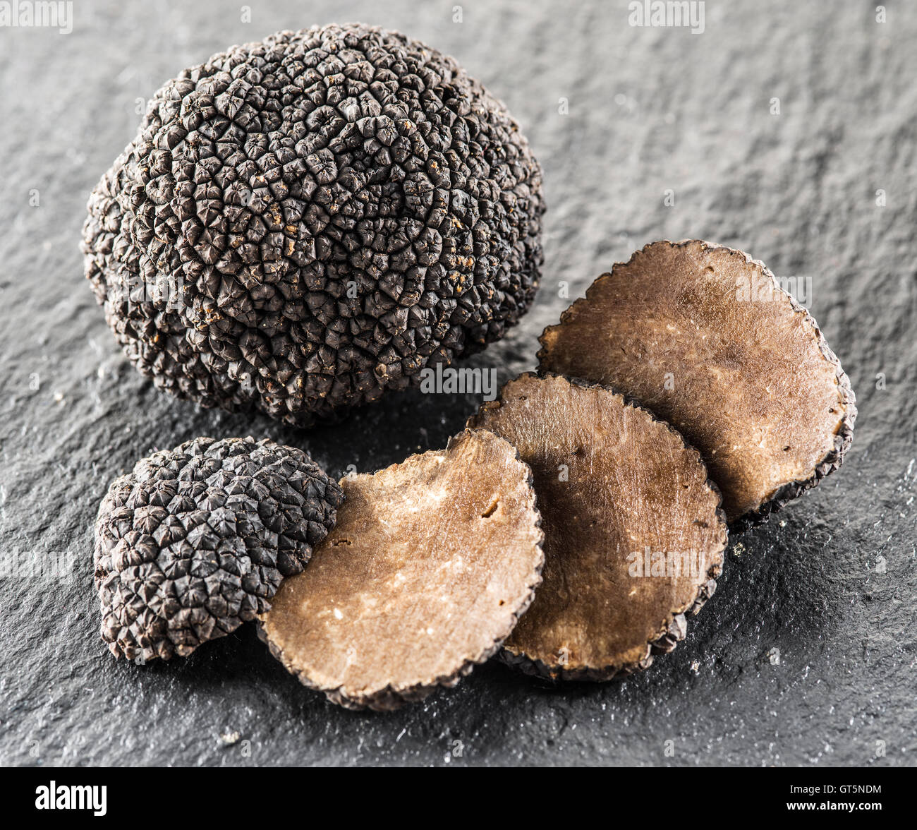 Black truffles and truffle slices on the graphite board. Stock Photo