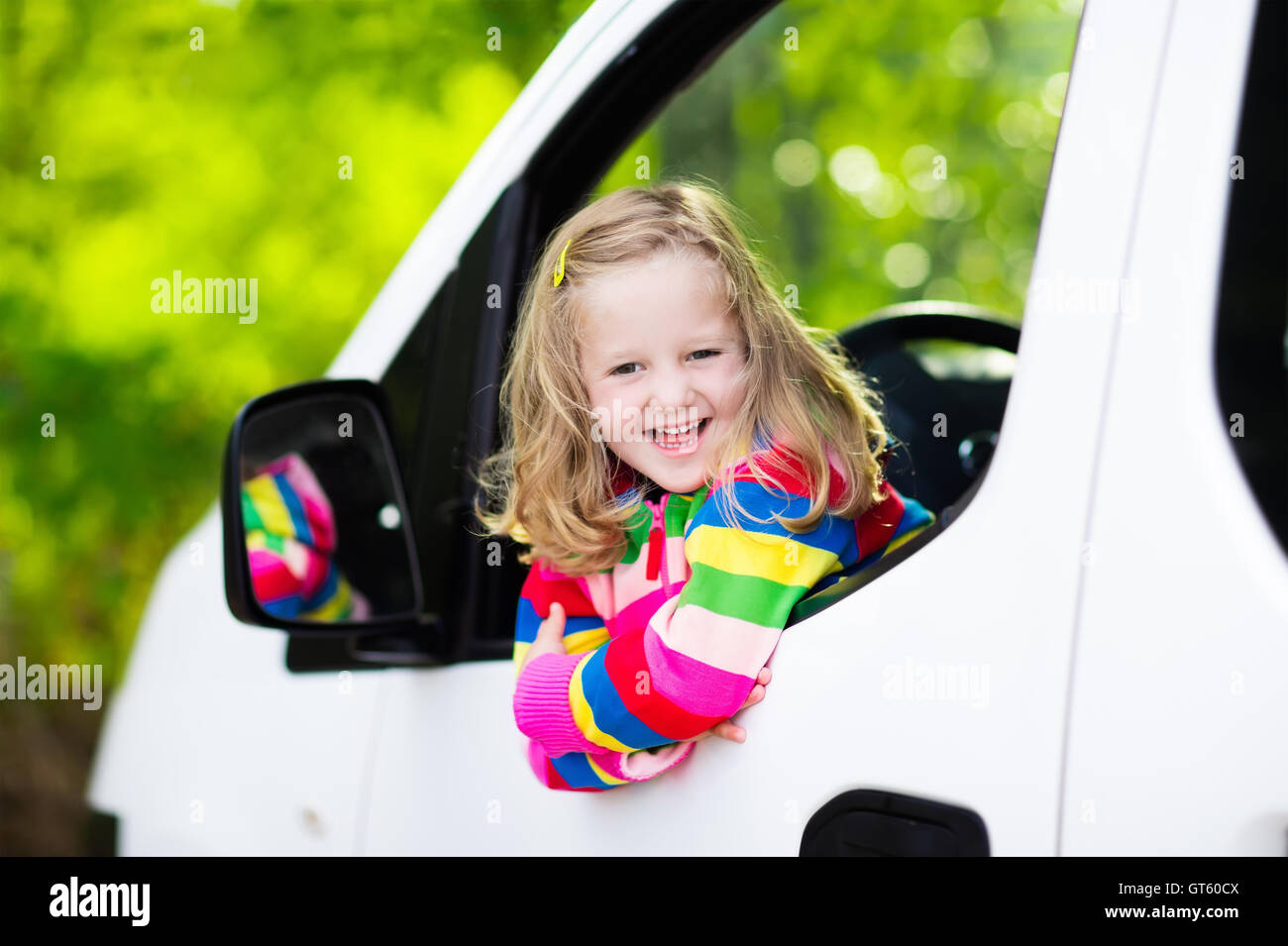 Little girl with funny pigtails watching out of car window sitting on front driver seat during a break on a family vacation trip Stock Photo