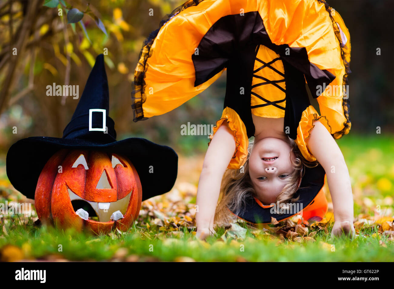 Little girl in witch costume playing in autumn park. Child having fun at Halloween trick or treat. Kids trick or treating. Stock Photo