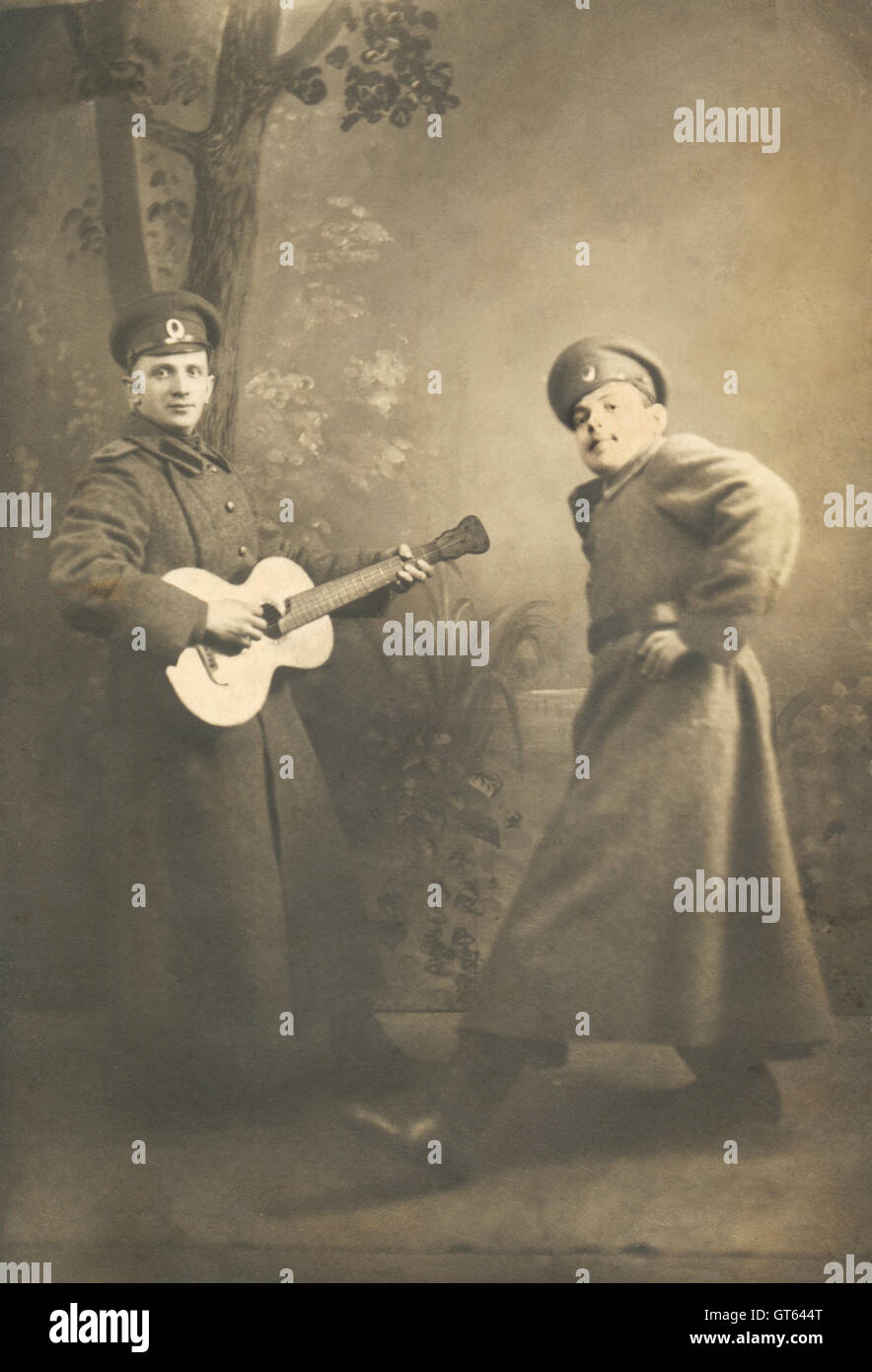 Vintage genre portrait of the two servicemen at the beginning of the twentieth century, Russia. Two young people in military uniform are playing a scene. One plays the guitar, the other is dancing Stock Photo