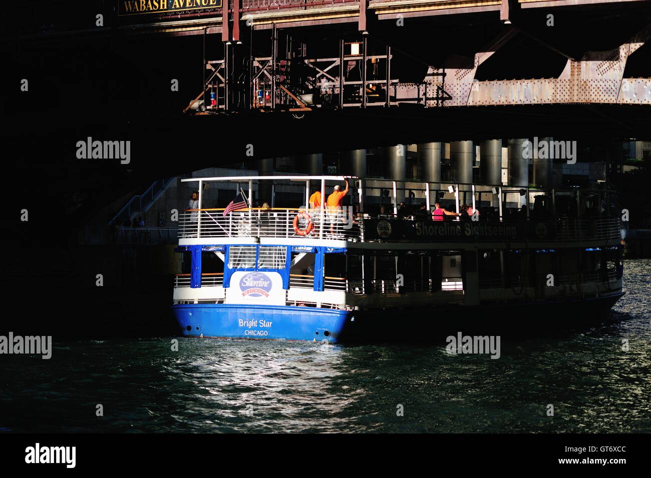 A Chicago water taxi/tour boat catches a sliver of late day light while passing under a bridge on the Chicago River. Chicago, Illinois, USA. Stock Photo