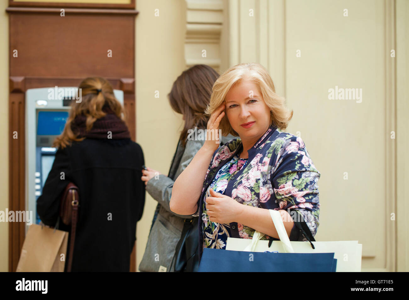 Mature blonde woman with credit card in hand near automated teller machine in shop Stock Photo