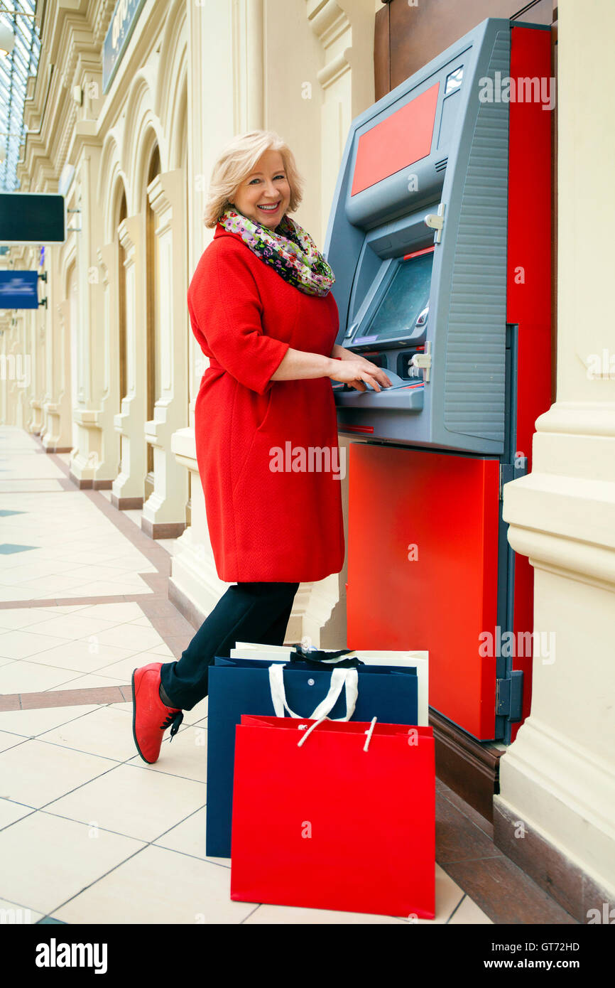 Mature blonde woman with shopping bags on the background of the ATM Stock Photo