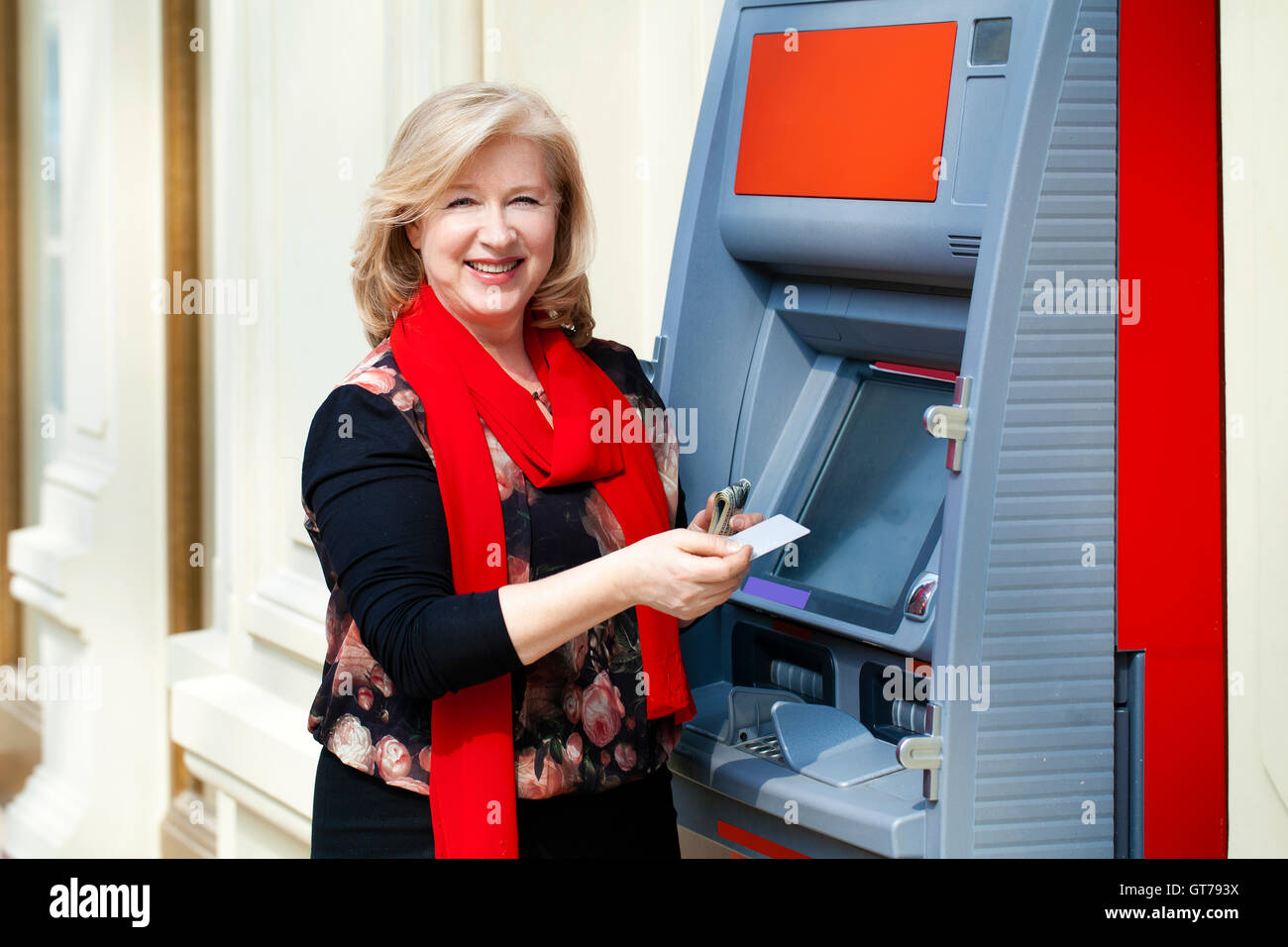 Mature blonde woman with credit card in hand near automated teller machine in shop Stock Photo