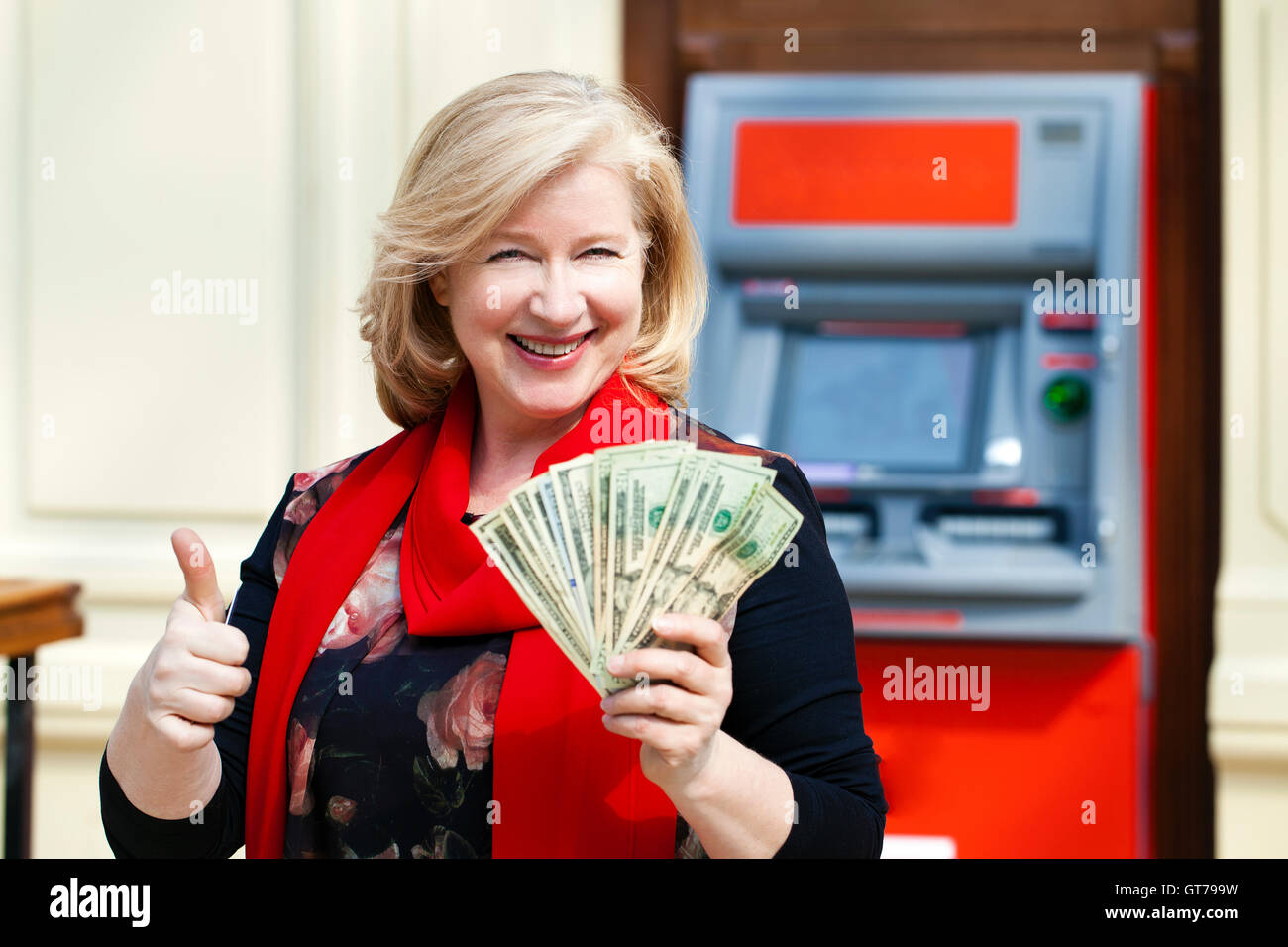 Mature blonde woman counting money near automated teller machine in shop Stock Photo