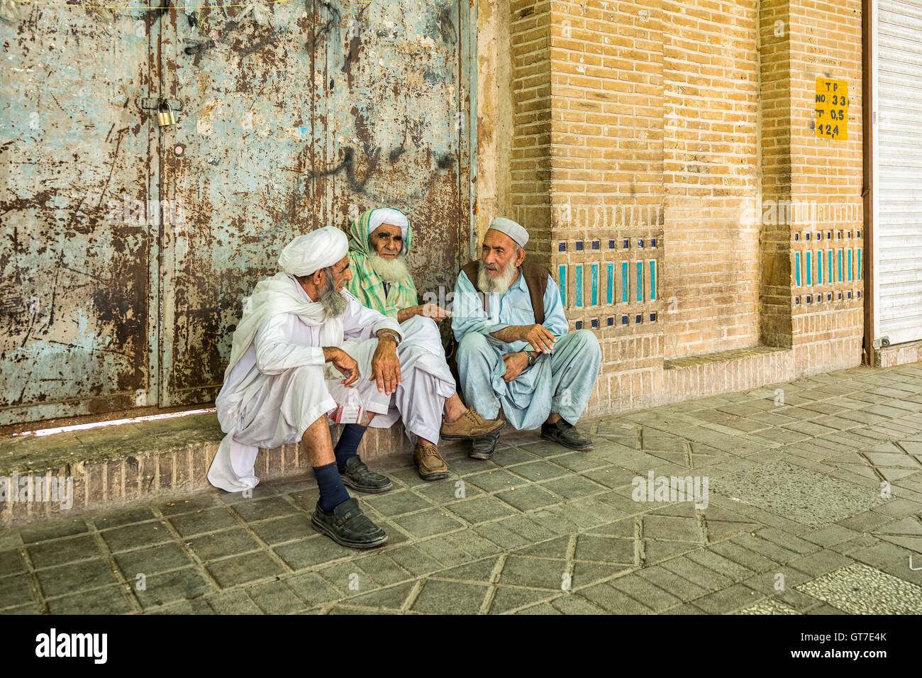 Iranian men wearing robes and turbans sitting on the sidewalk and talking in Yazd, Iran. Stock Photo