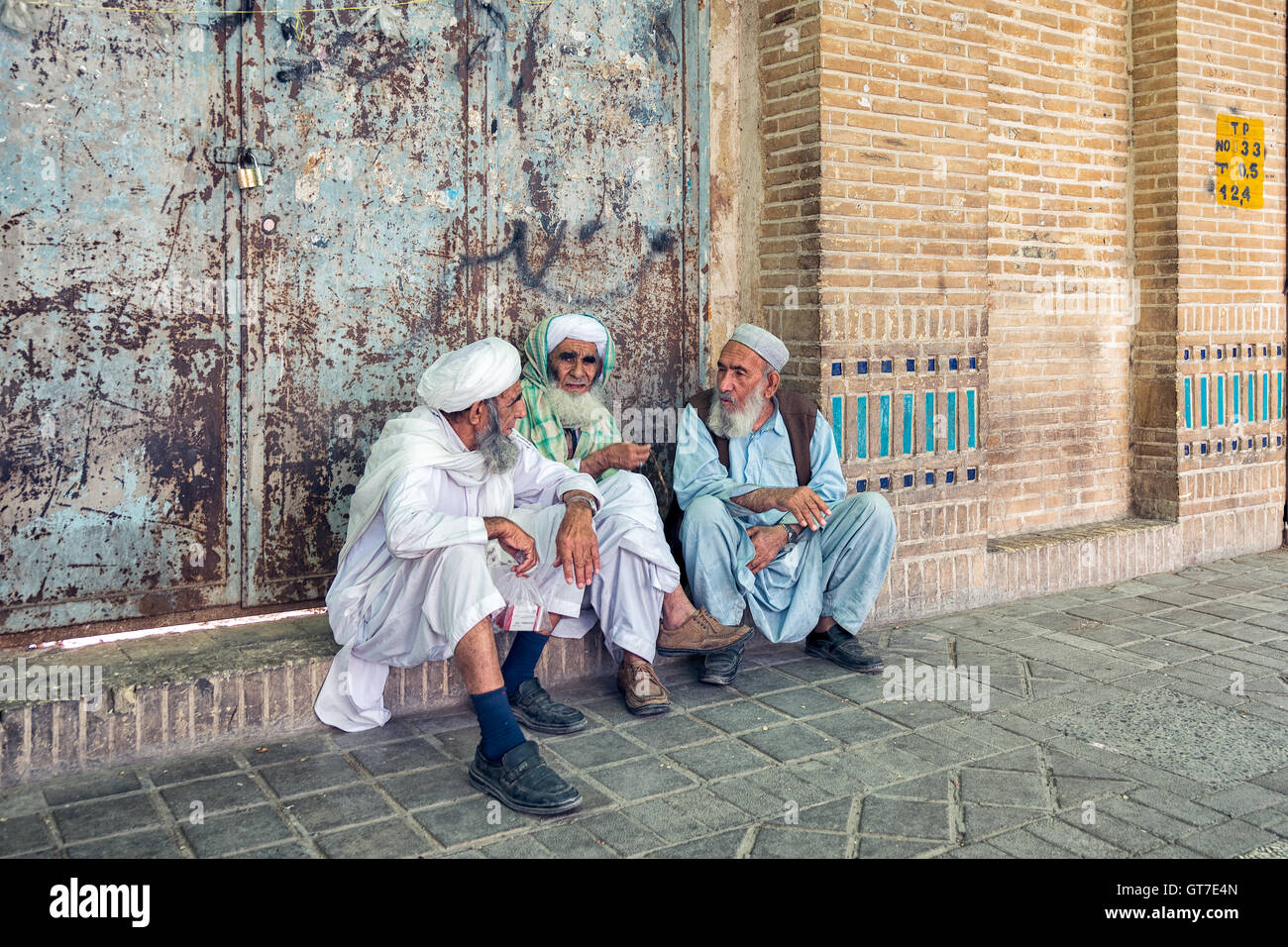 Iranian men wearing robes and turbans sitting on the sidewalk and talking in Yazd, Iran. Stock Photo