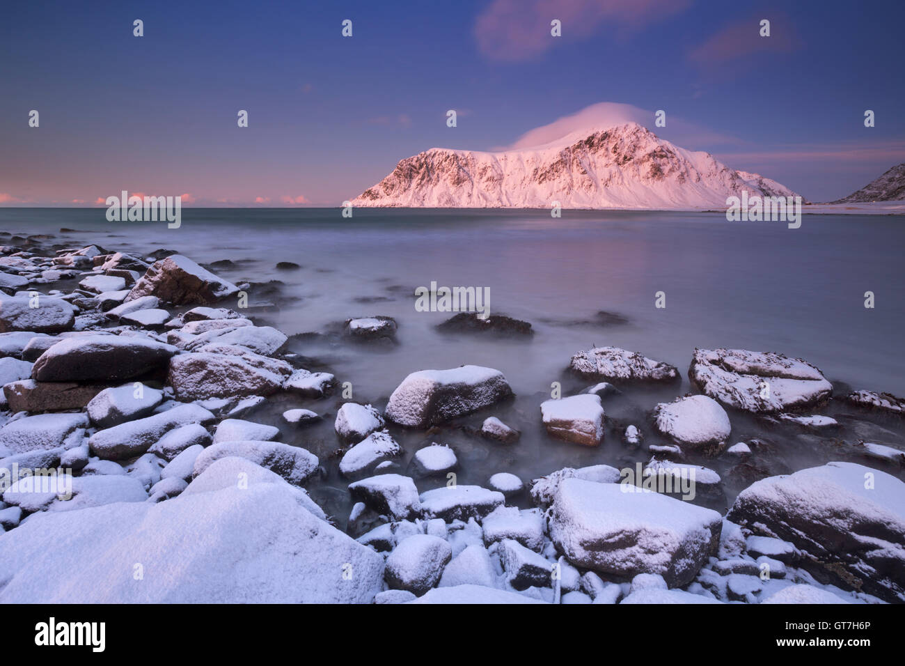 Alpenglow at the rocky beach of Skagsanden on the Lofoten in northern Norway, photographed at dusk in winter. Stock Photo
