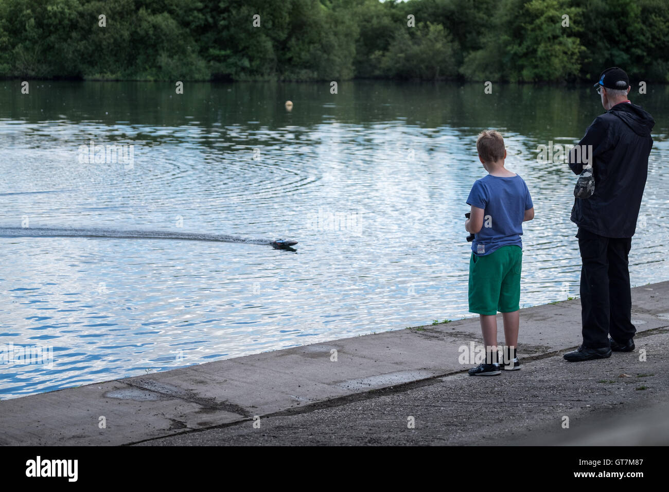 Grandfather and grandson playing with a model powerboat on a lake Stock Photo