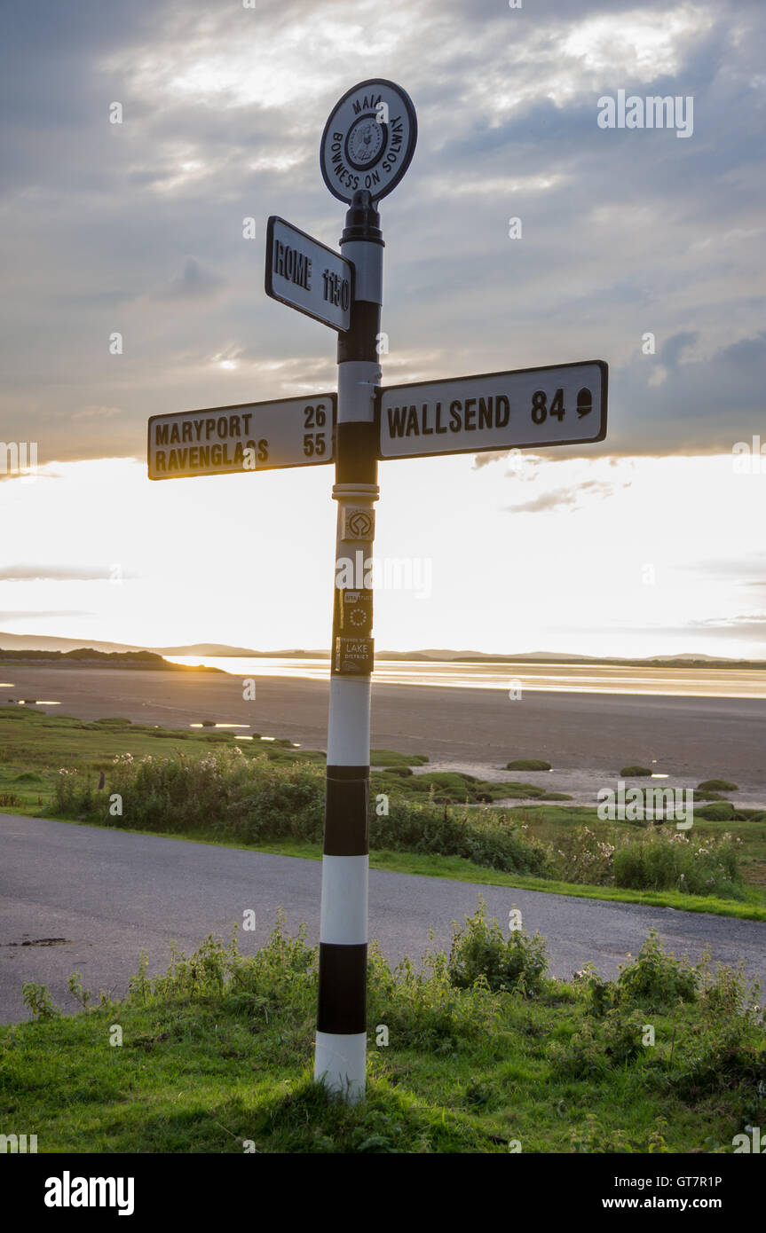 Fingerpost sign showing distances to Wallsend, Maryport and Rome, Solway Firth at sunset, Bowness-on Solway, Cumbria, England Stock Photo