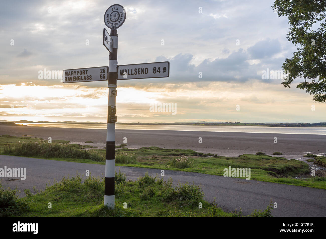 Fingerpost sign showing distances to Wallsend, Maryport and Rome Solway Firth at sunset, Bowness-on Solway, Cumbria, England Stock Photo