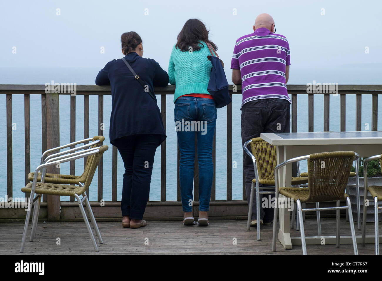 Three people stand on a balcony overlooking the sea. Stock Photo