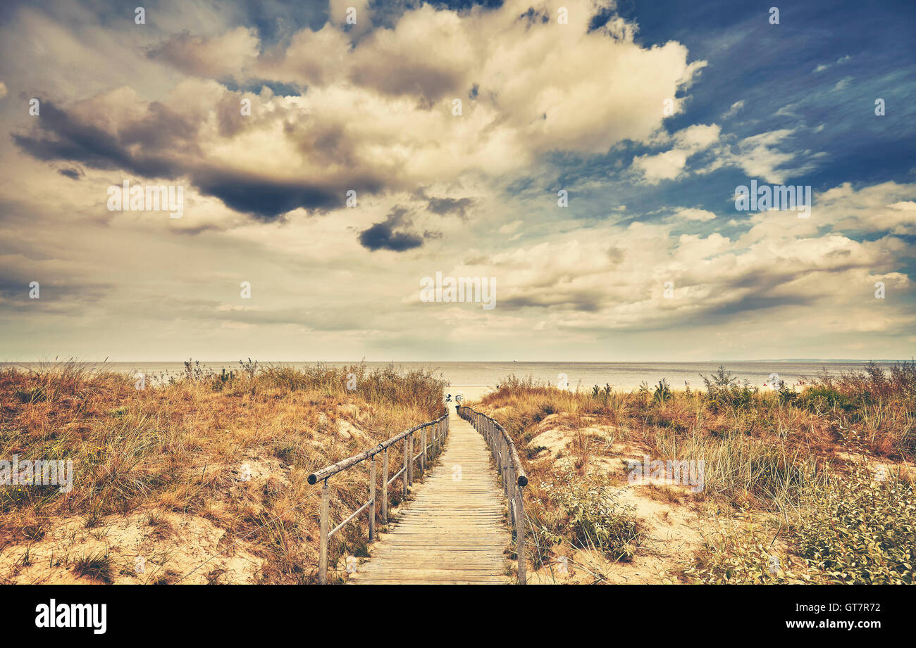 Retro toned wooden footpath leading to a beach in a cloudy day. Stock Photo