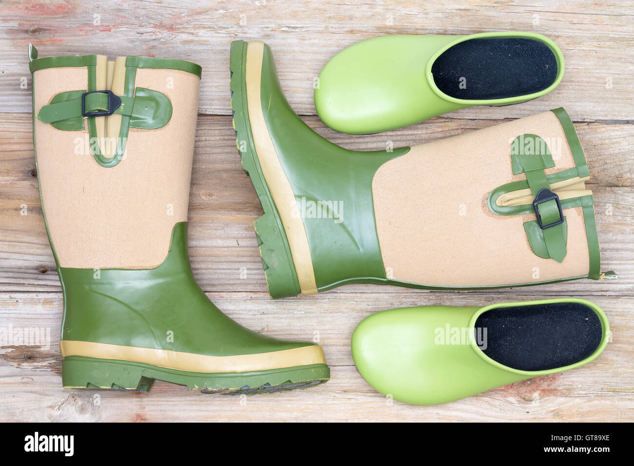 Stylish footwear for a fashionable gardener with green and beige decorative gumboots and green clogs lying on rustic wooden boar Stock Photo