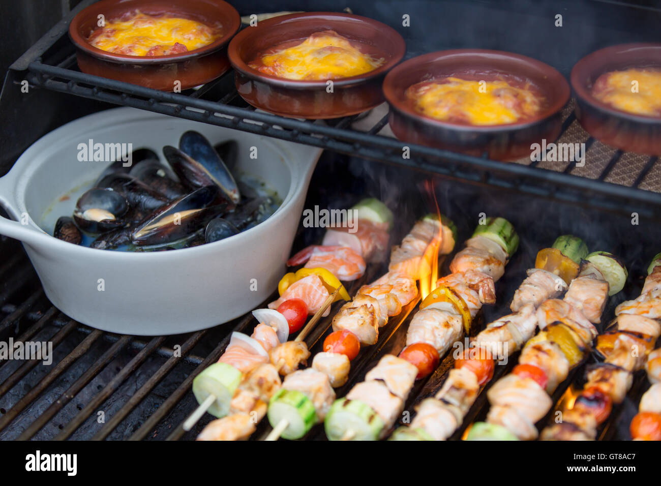 Delicious seafood outdoor meal at the BBQ with grilled salmon shish kebabs, marine mussels and individual pots of sausage stew, Stock Photo