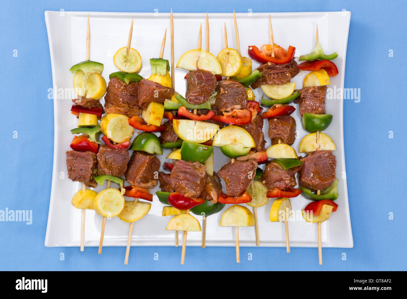 Tasty spicy marinated meat and vegetable kebabs displayed on a platter on their skewers ready for the summer barbecue, overhead Stock Photo