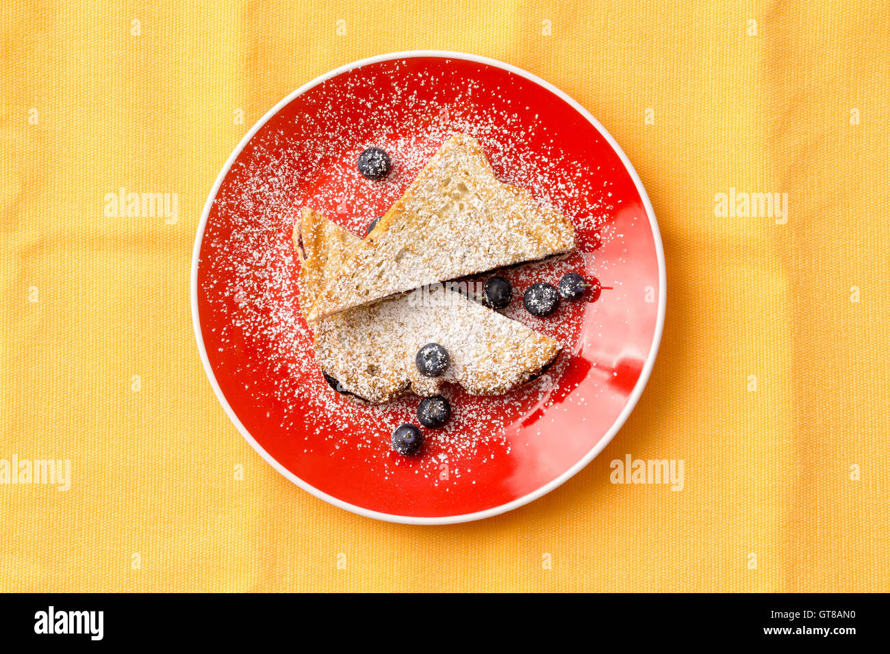 Aerial Shot of a Tasty French Toast Bread with Strawberry Jam Filling on Round Red Plate with Blueberry Fruits. Isolated on Yell Stock Photo