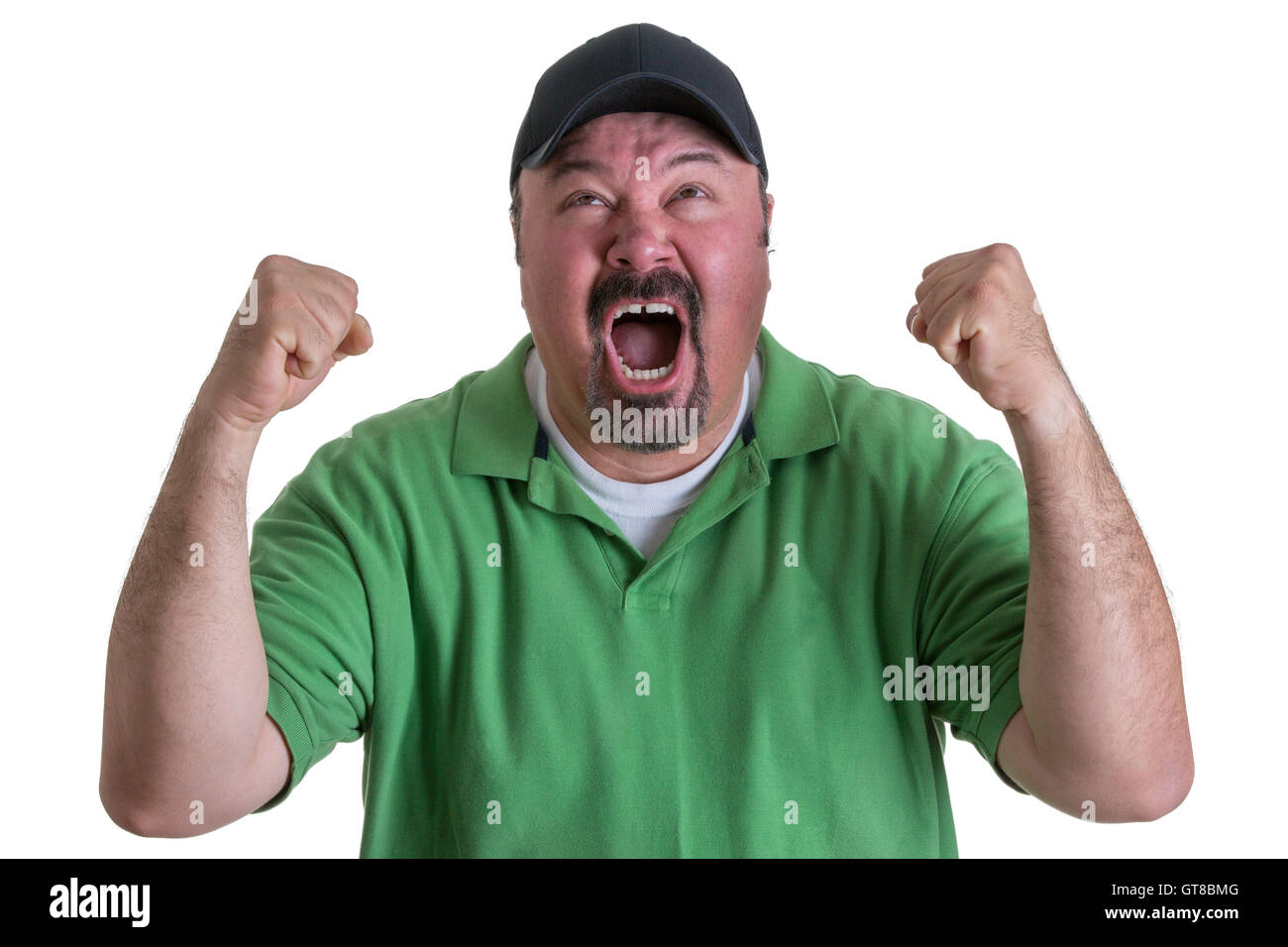 Excited Overweight Man Wearing Green Shirt and Black Baseball Cap Celebrating, Pumping Fists and Cheering in Studio with White B Stock Photo