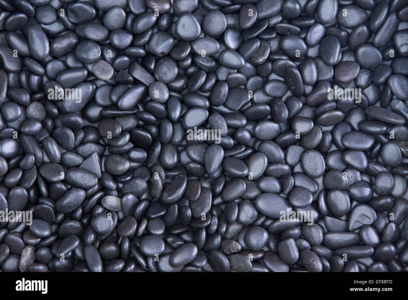 Background texture of small smooth waterworn black pebbles or stones for use in decor and garden landscaping, full frame close u Stock Photo