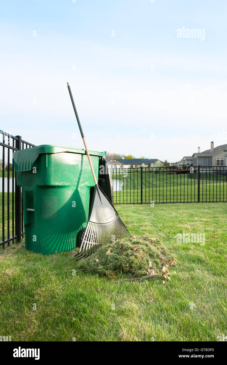 Yard maintenance in spring cleaning the lawn and raking up grass clippings after mowing with a pile of grass and rake leaning on Stock Photo