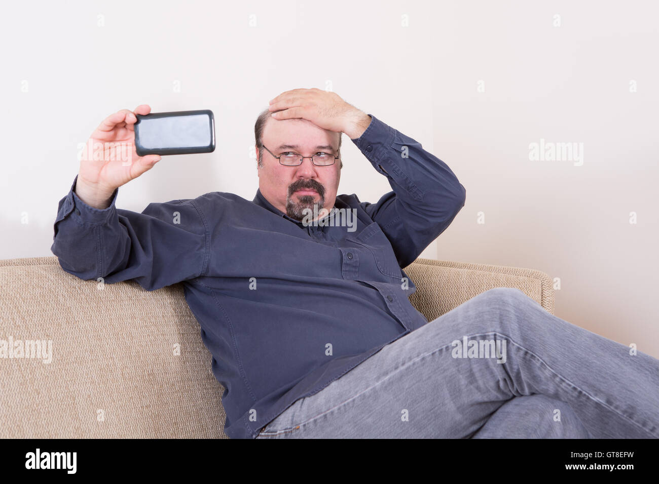 Vain man taking a selfie on his smartphone checking his hair with his hand as he looks critically at the screen while seated on Stock Photo