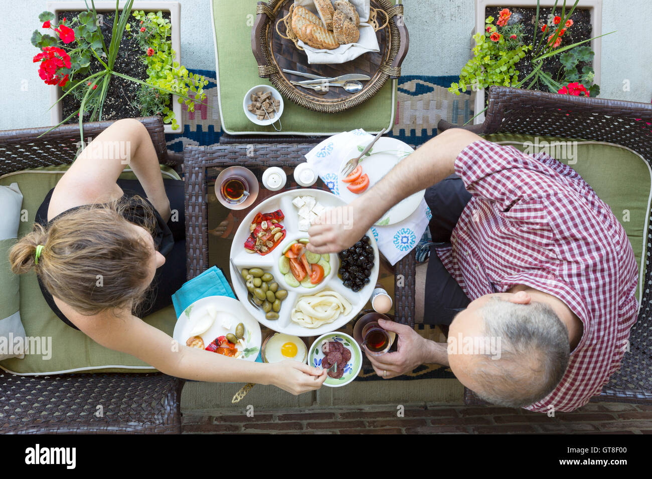 Man and woman enjoying an outdoor Turkish breakfast sitting together at a small intimate table helping themselves to a selection Stock Photo