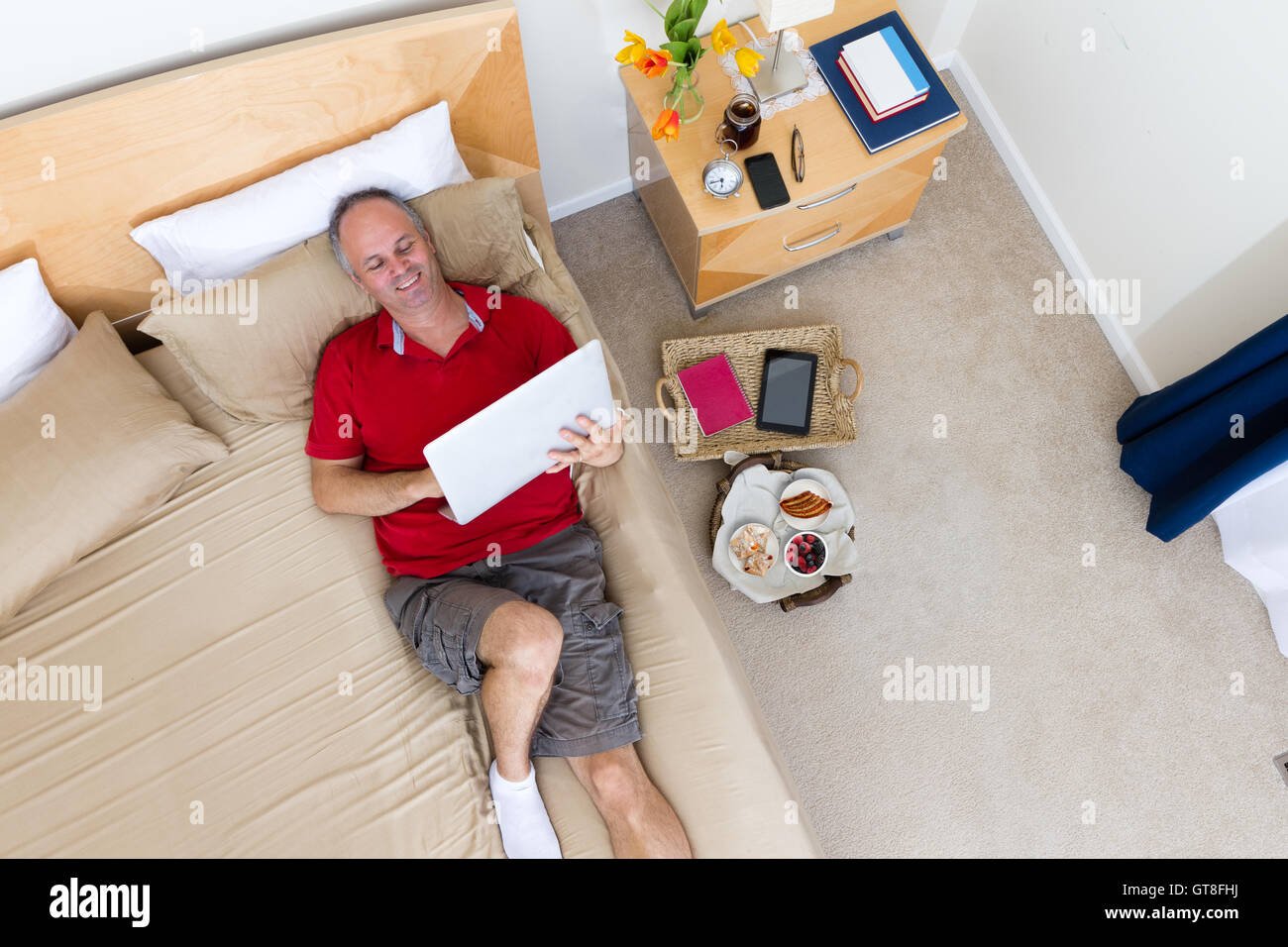 https://c8.alamy.com/comp/GT8FHJ/high-angle-view-of-smiling-mature-man-lying-on-bed-with-laptop-in-GT8FHJ.jpg