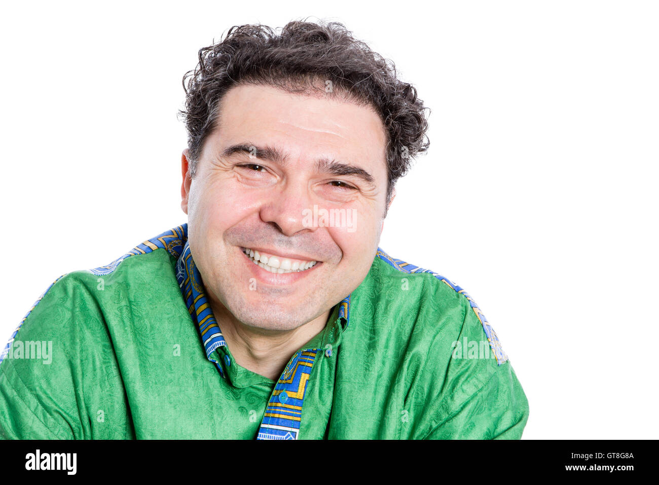 Happy handsome man with curly brown hair wearing a green afro shirt looking at the camera with a wide beaming smile of pleasure Stock Photo