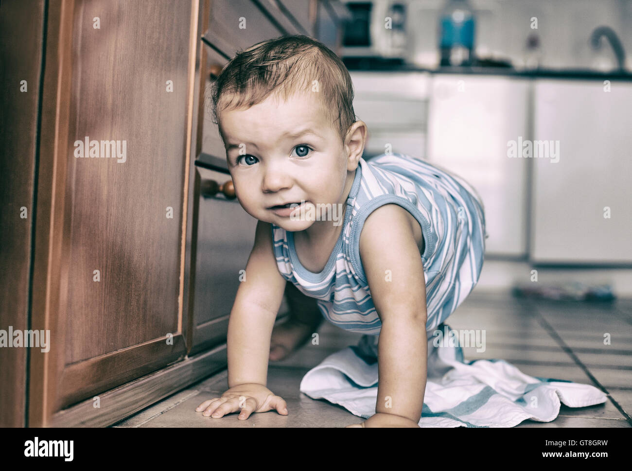 Happy baby boy crawling in the kitchen. Vintage filtered Stock Photo