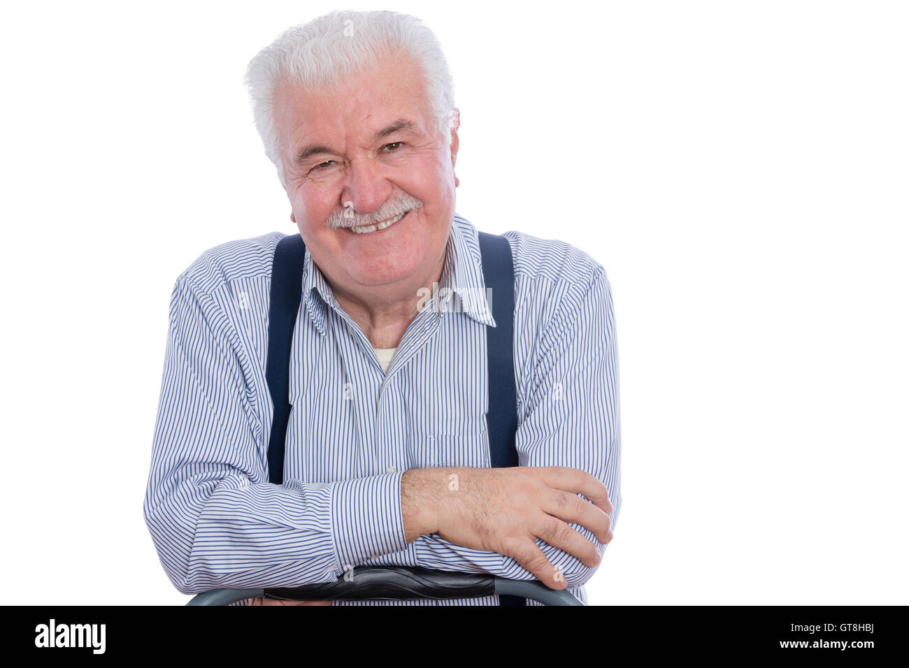 Cute senior man with mustache in white striped shirt and blue suspenders with joyful expression and folded arms over white backg Stock Photo