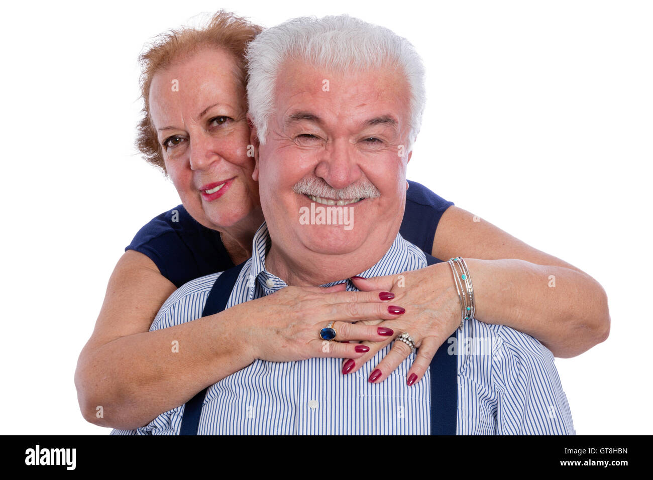 Smiling husband in pinstripe shirt with suspenders being hugged by happy wife from behind over white background Stock Photo