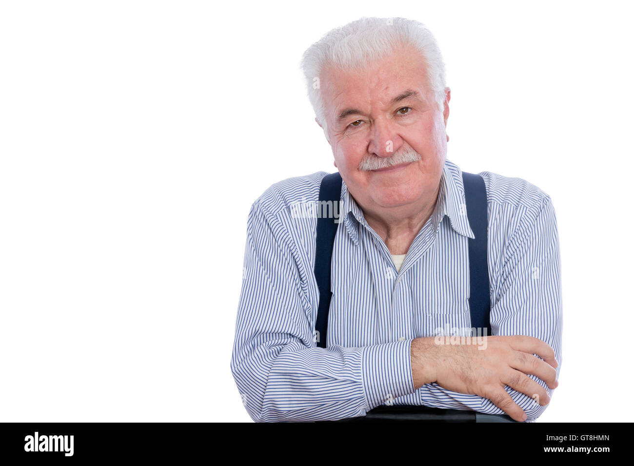 Handsome senior man in white striped shirt and blue suspenders with calm expression and folded arms Stock Photo