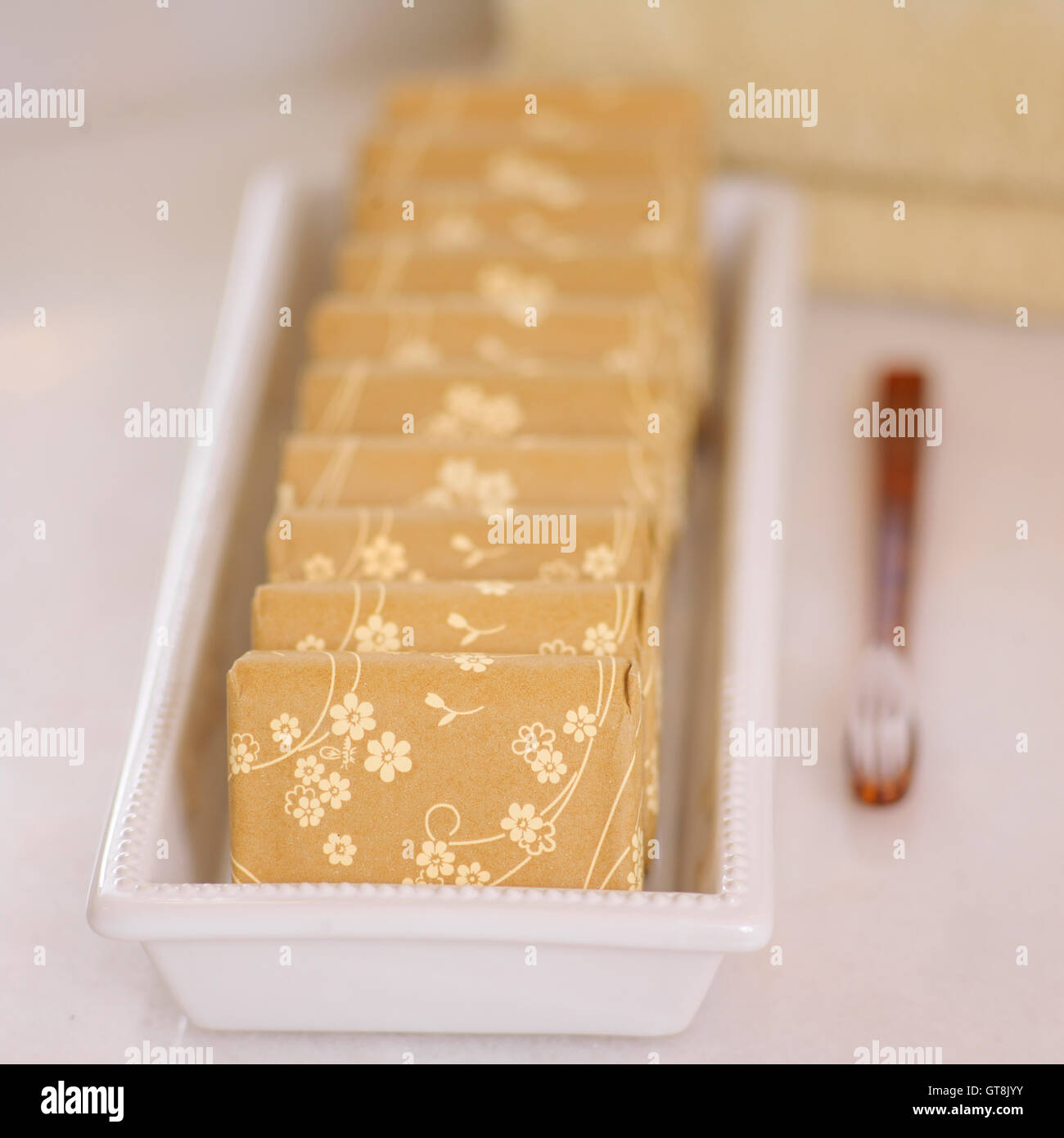 Close-up of Floral Wrapped Bars of Soap in Dish with Towels and Toothbrush Stock Photo