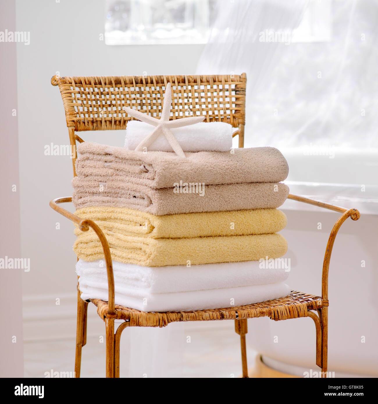 Stack of Fresh Towels and Starfish on Wicker Chair in Bathroom Stock Photo