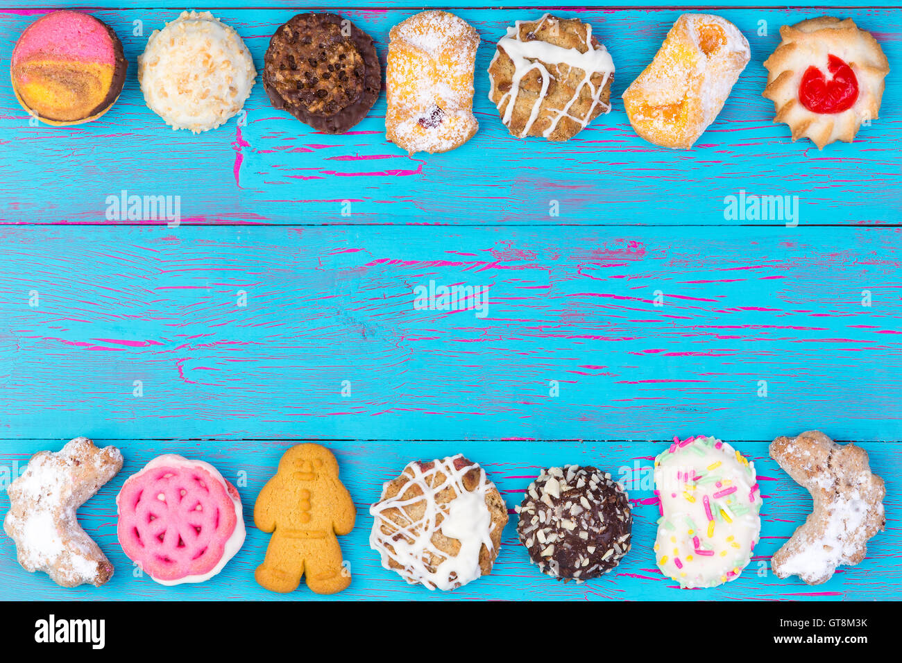 Double border of colorful cookies or biscuits arranged in a line on a turquoise blue crackle paint wooden background, overhead v Stock Photo