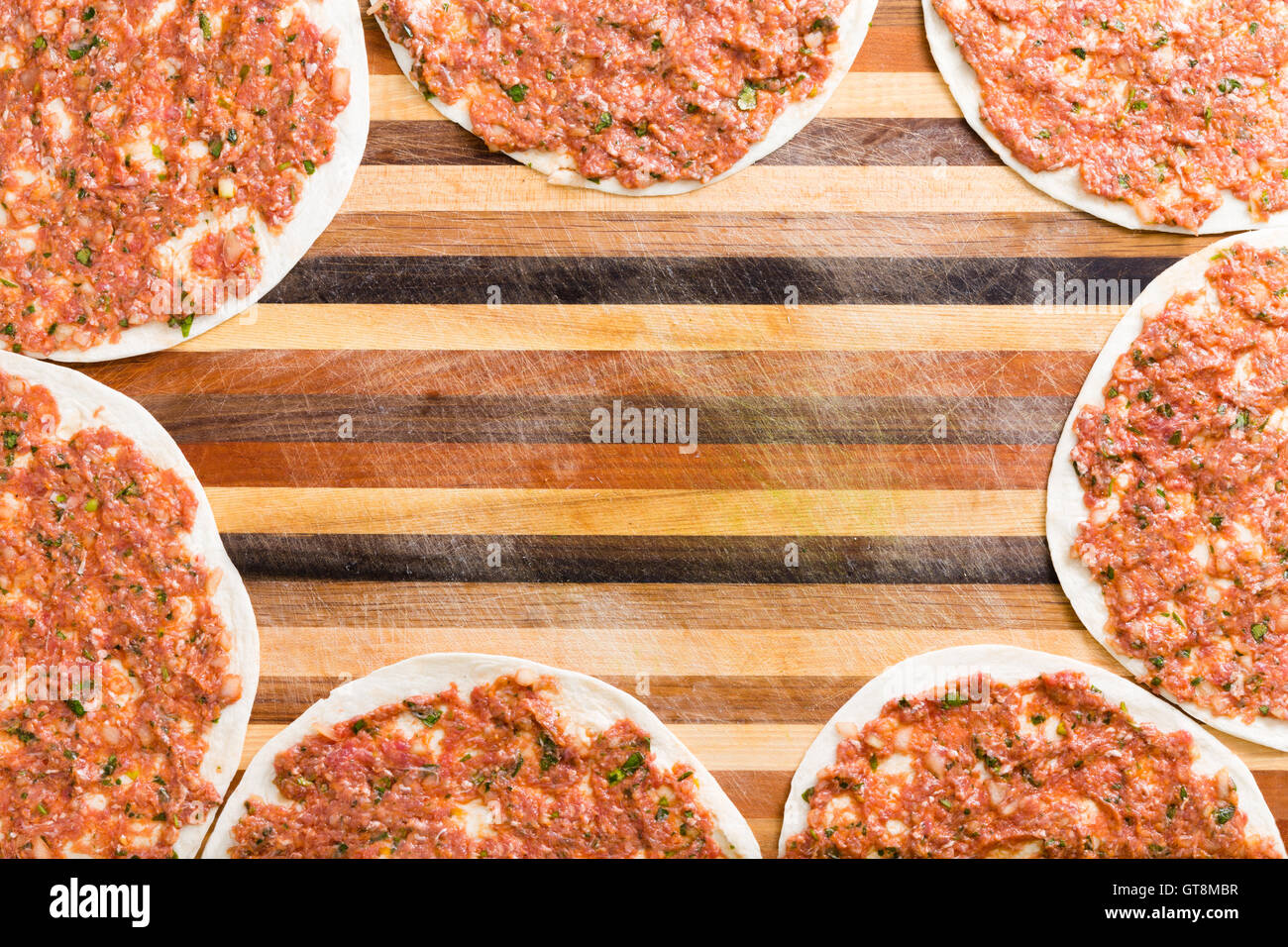 Frame of ready to cook traditional Turkish lahmacun on a decorative wooden board with colorful inlaid stripes and central copysp Stock Photo