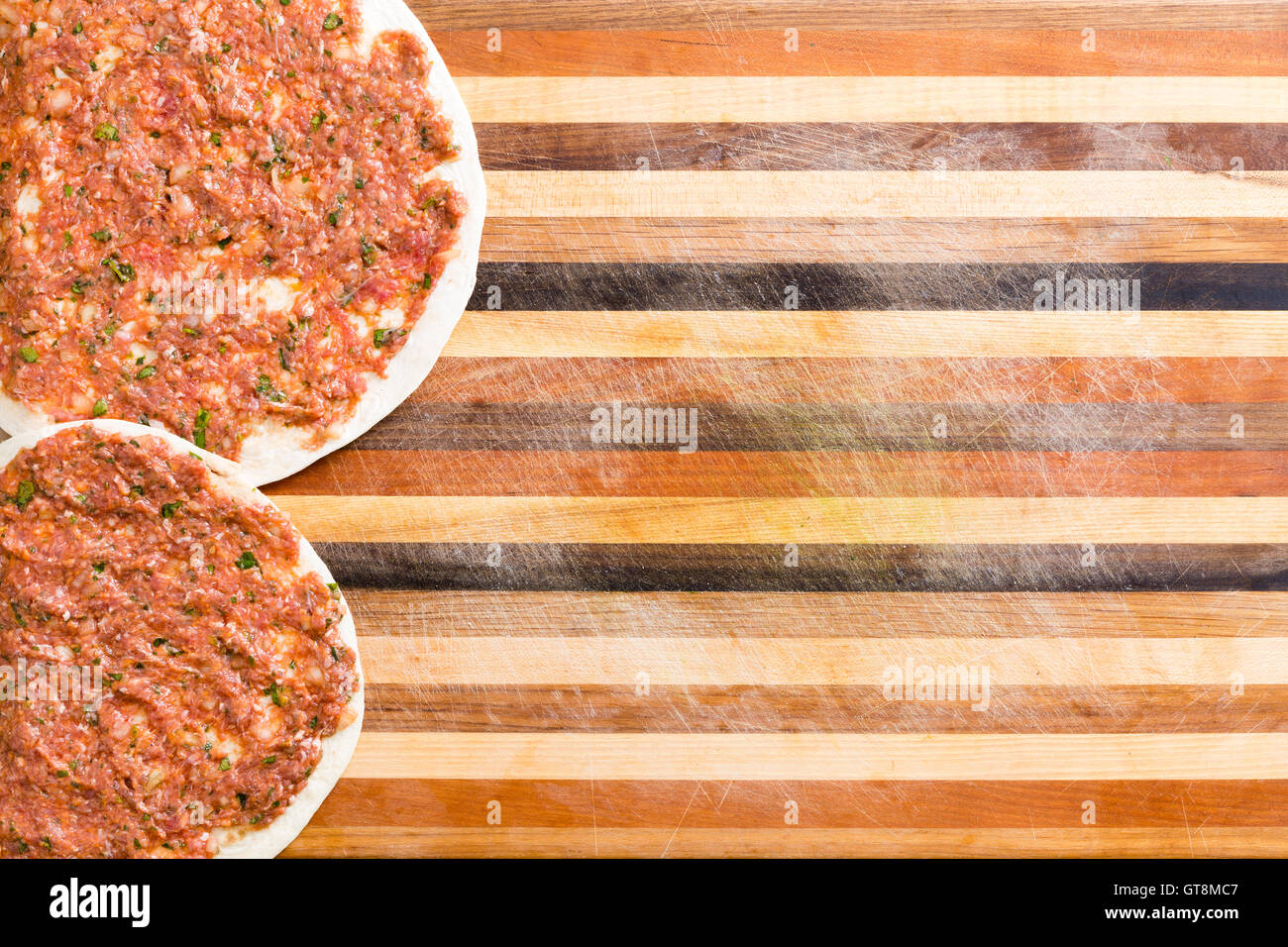 Two prepared Turkish lahmacun with a savory minced meat and veggie mix on a dough base ready to cook forming a side border on a Stock Photo