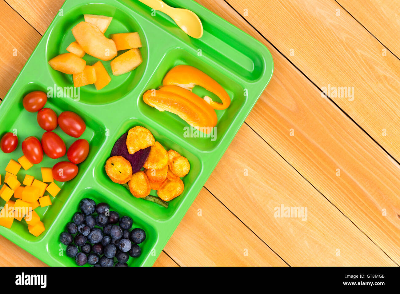 Child size lunch tray with cherry tomatoes, melon, blueberries and sweet pepper fruit on wooden table Stock Photo