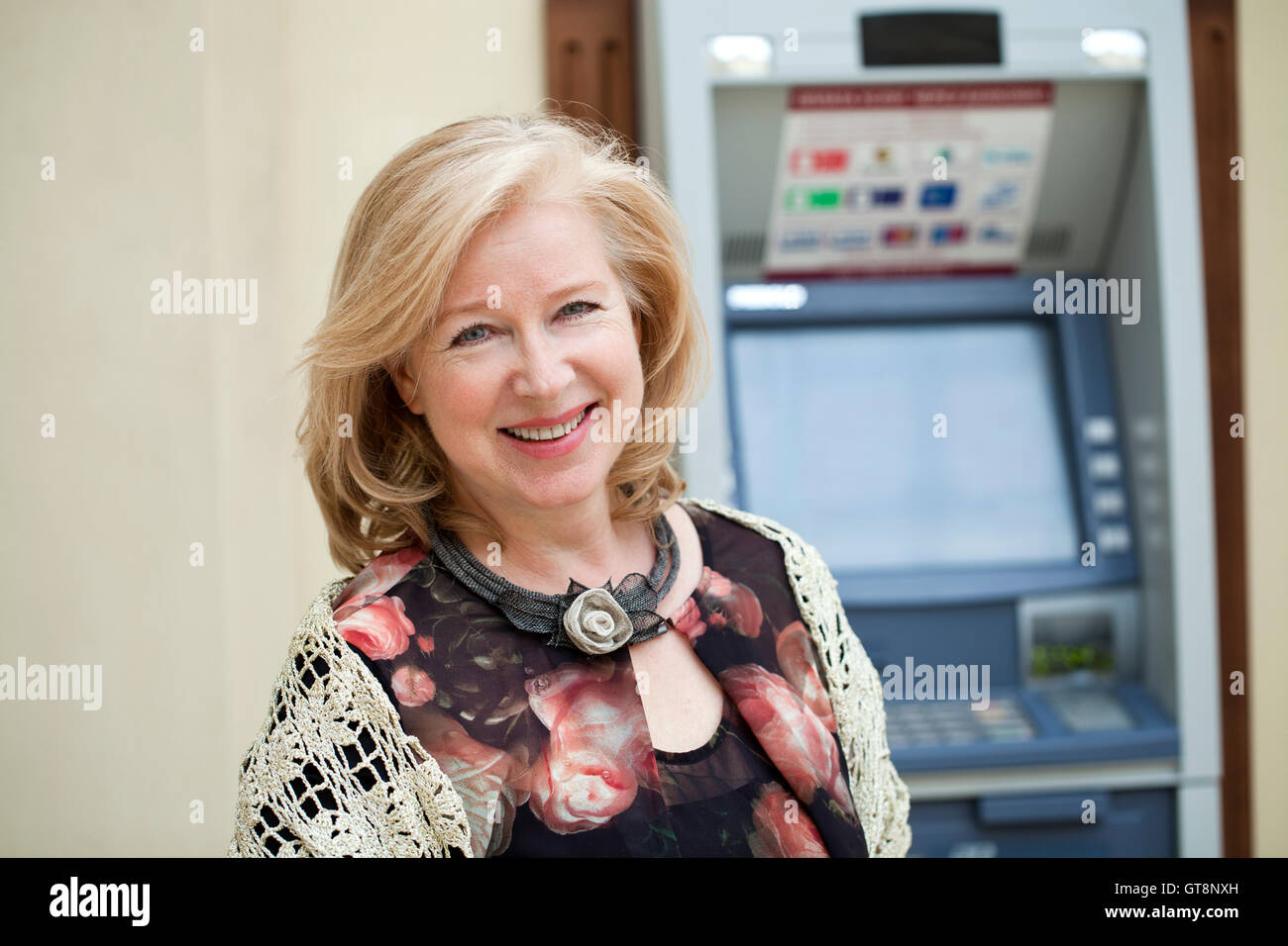 Happy Mature blonde woman near automated teller machine in shop Stock Photo