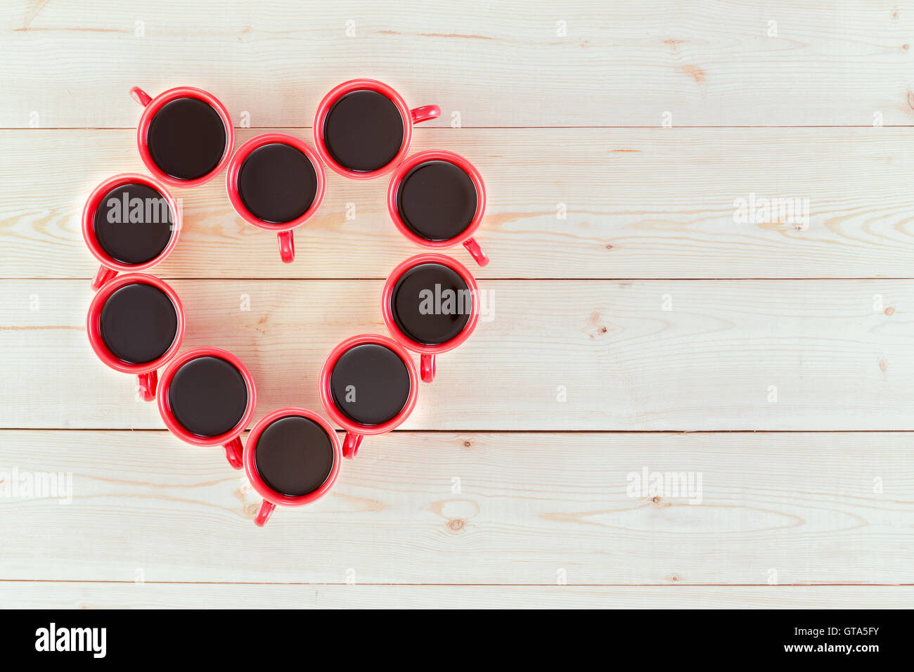 Coffee makes you happy concept with freshly brewed espresso coffee in red mugs arrabged in a heart shape over white boards with Stock Photo