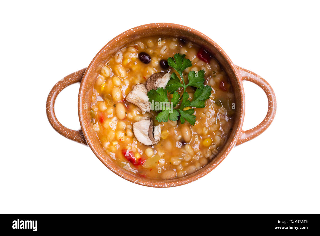 Overhead view of hearty bean and vegetable soup cooked in a clay pot against a white background Stock Photo