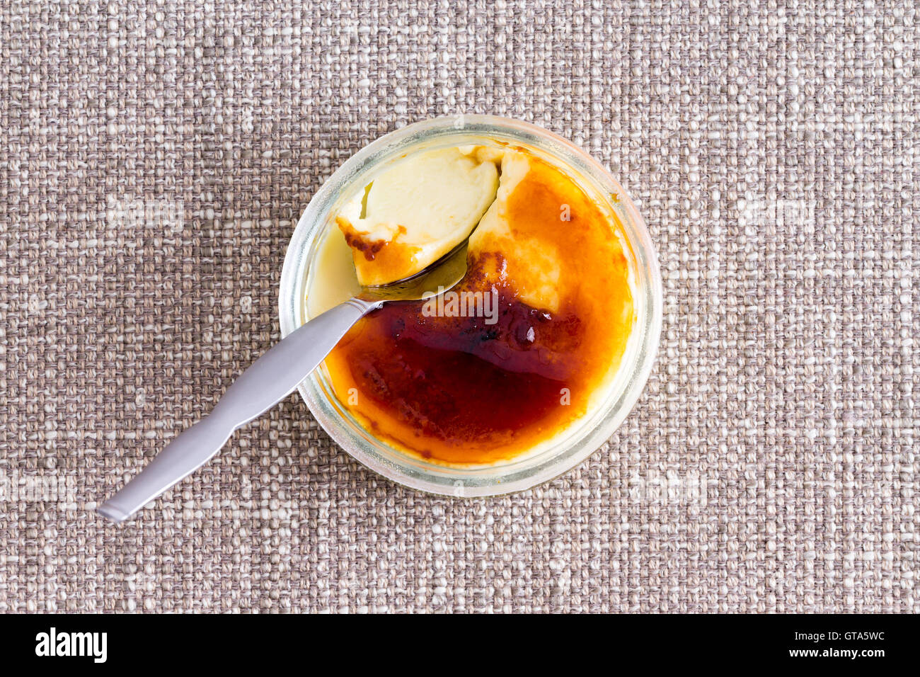 Partially eaten browned creme brulee with silver spoon against a textured background Stock Photo
