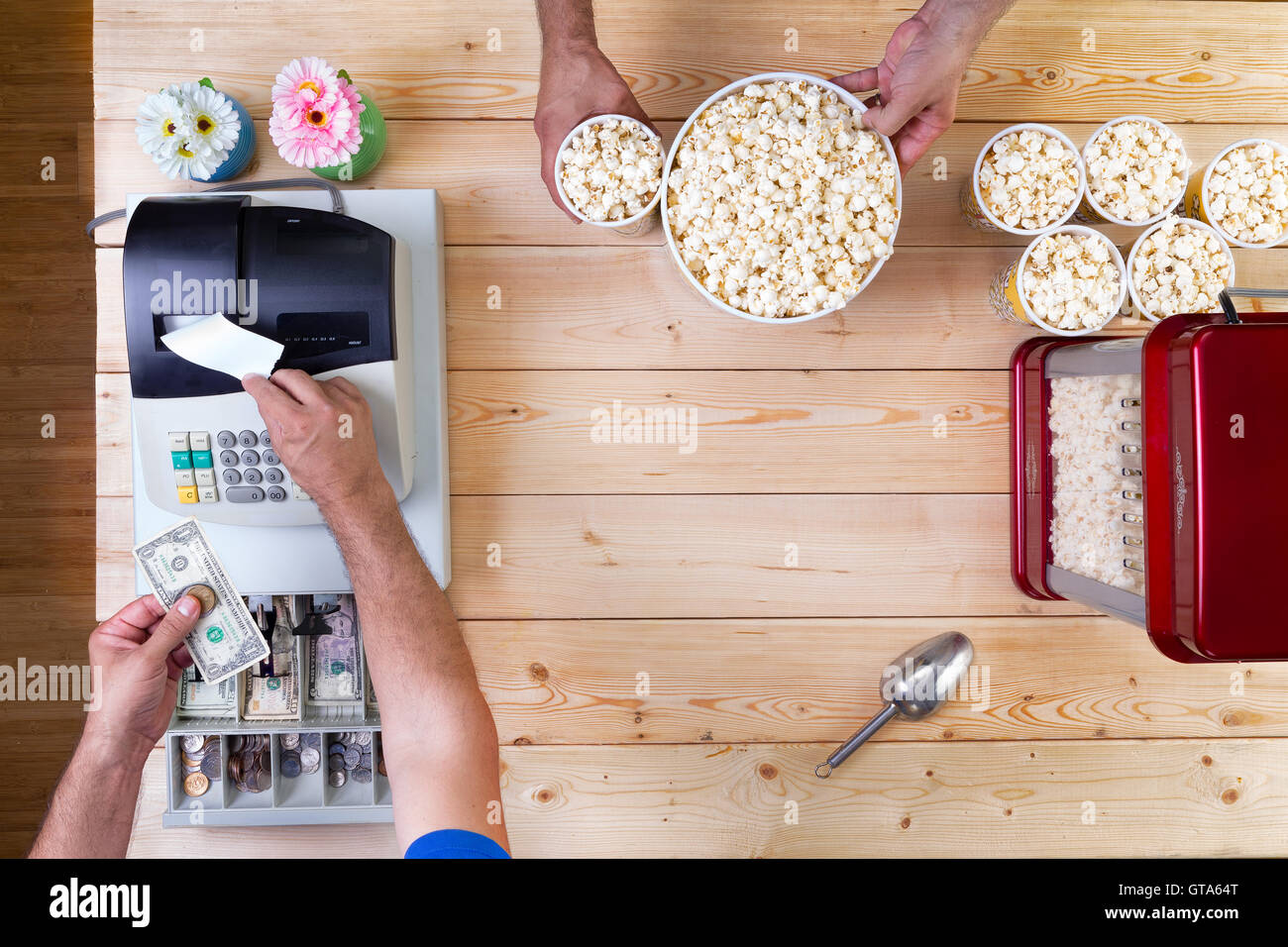 Man selling freshly made bowls of popcorn tendering money at the cash register for a customer, overhead view of their hands and Stock Photo