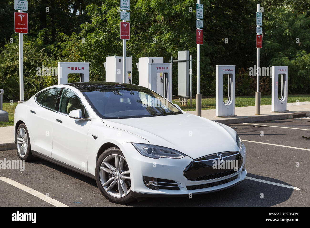 A Tesla Model S automobile gets a charge from a Tesla supercharger charging station at a highway rest stop. Stock Photo