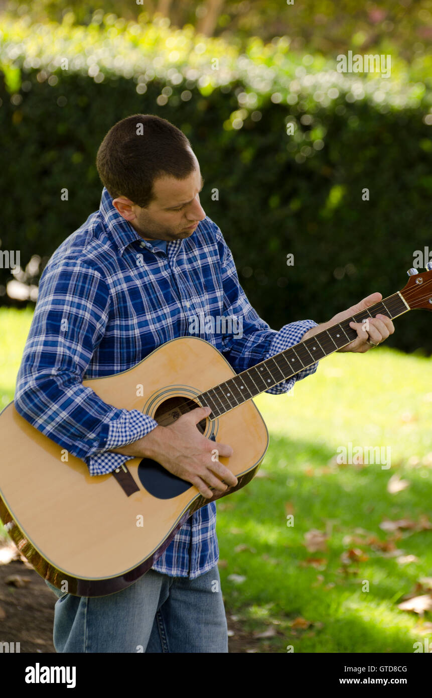 Man playing acoustic guitar outdoors in a park. Stock Photo