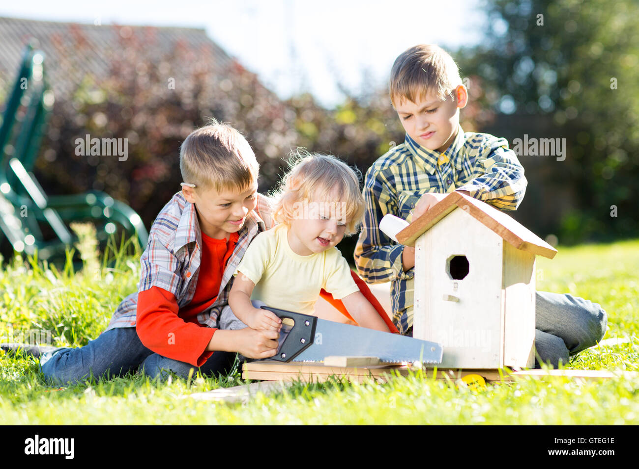 Happy kids making wooden birdhouse by hands. Older child teaches his younger brother. Stock Photo