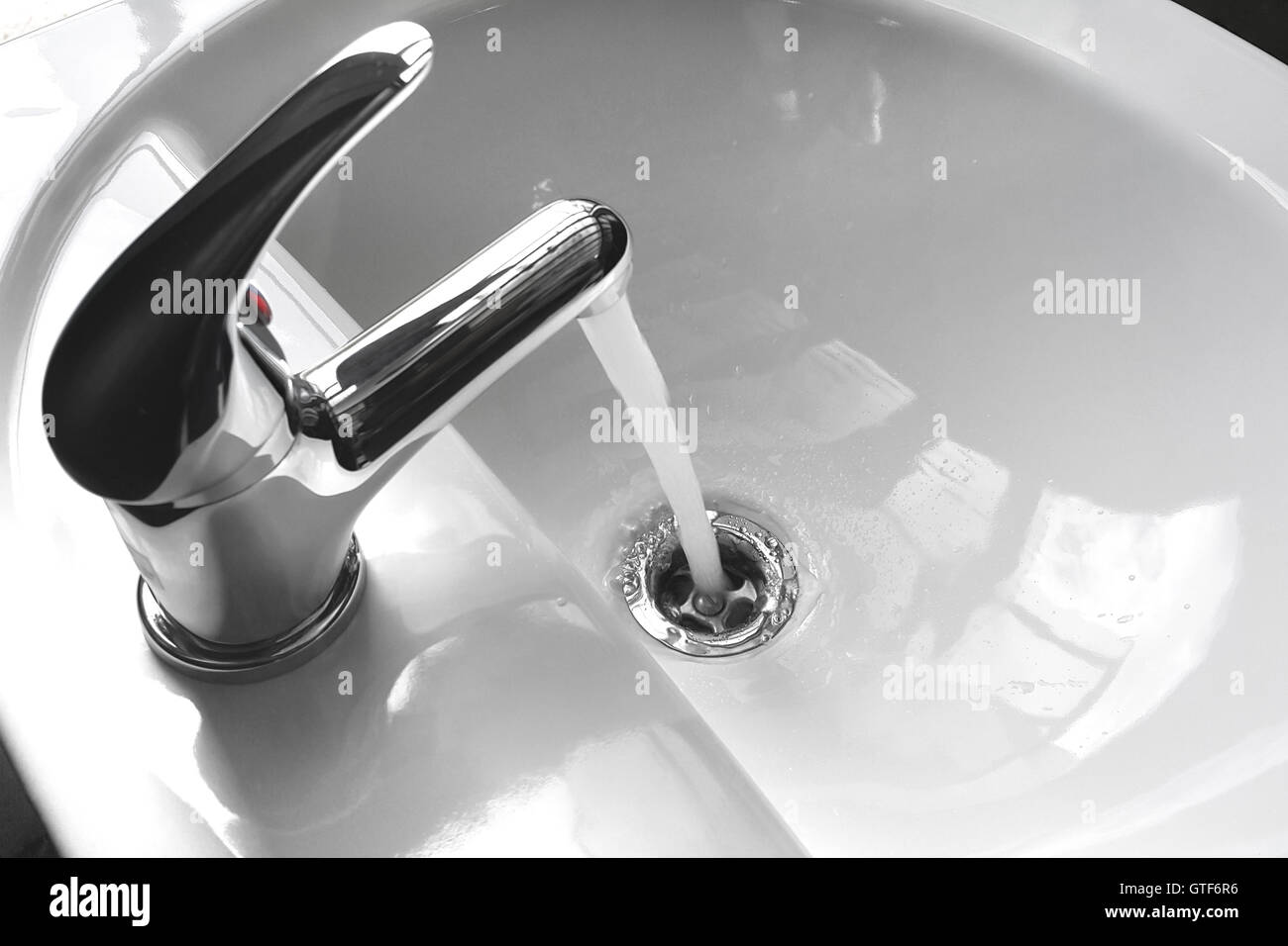 Water tap faucet with flowing water in a white bathroom sink. Stock Photo
